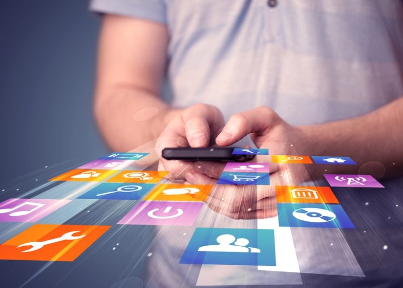 A man using his mobiel phone apps|A lady uses her phone as walking down the street|A graphic of two smartphones with hands holding beer coming out the screens to cheers