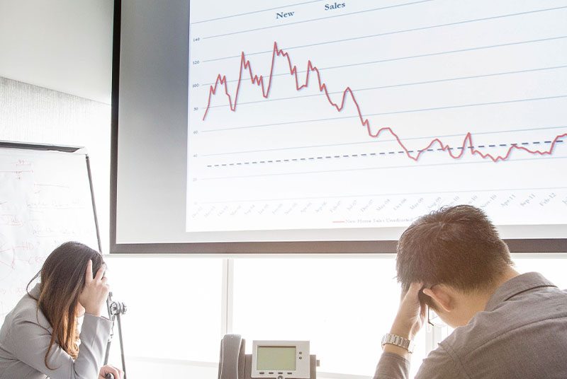 Two colleagues sit sadly with head in hands at a graph showing a slump in sales.
