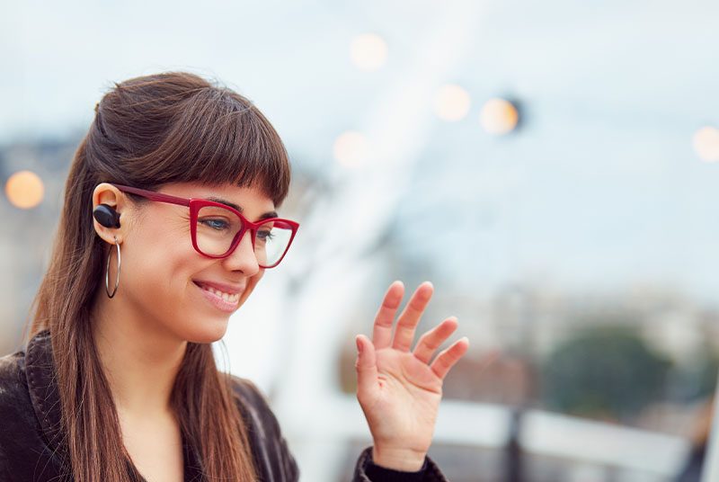 A lady waves at an online meeting whilst sitting outside.